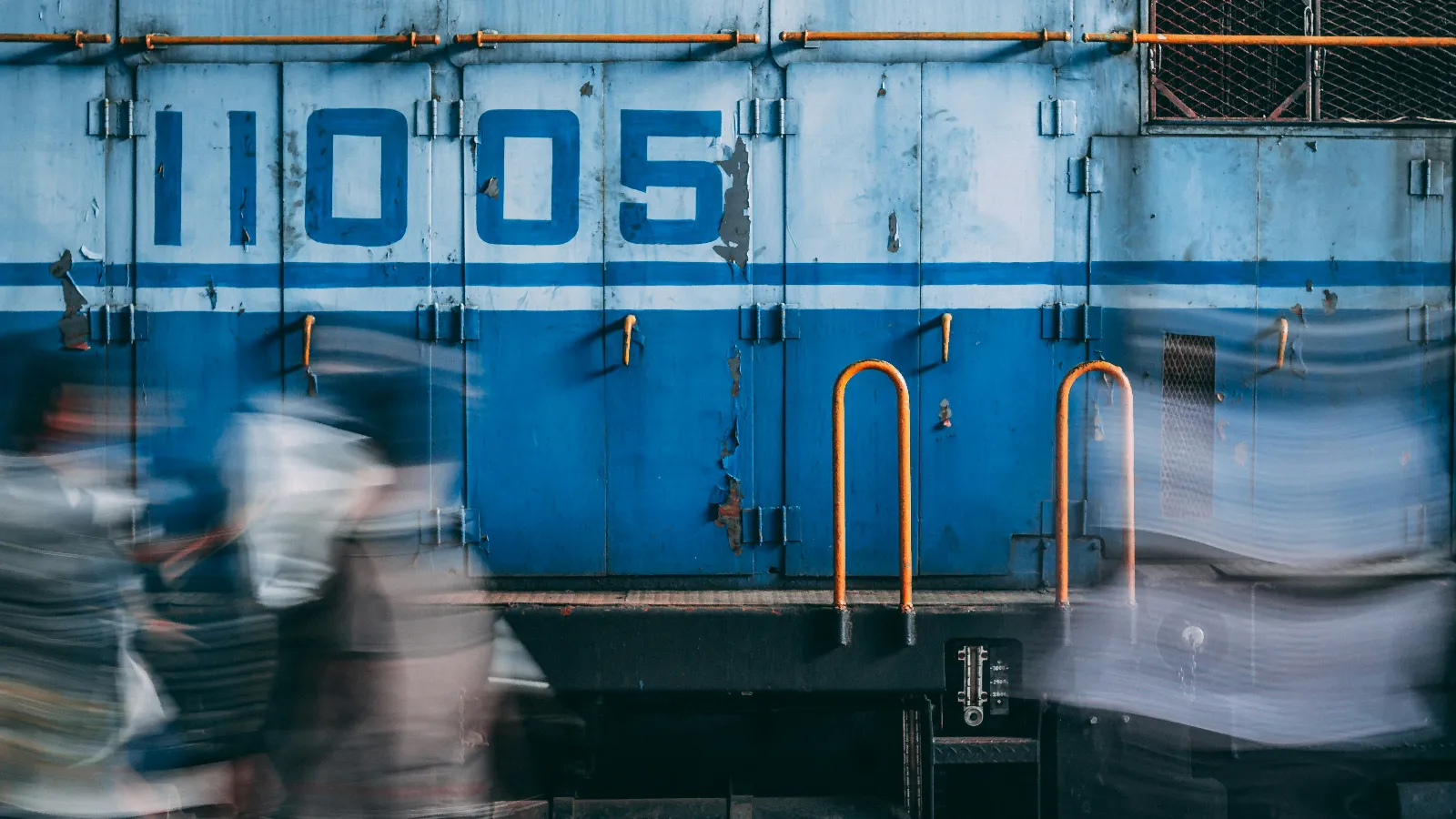 Blurred people walking past blue train